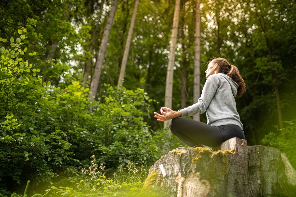 Eine Frau meditiert auf einem Baumstumpf im Wald