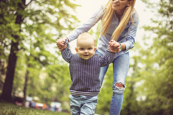 Kleinkind macht erste Schritte im Wald an Mamas stützenden Händen